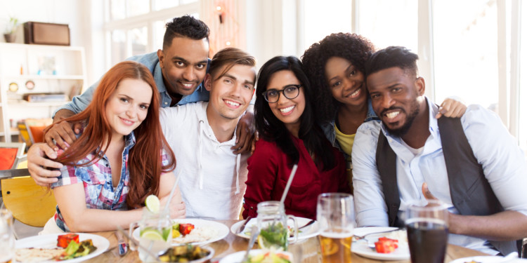 leisure, food and people concept - group of happy international friends eating at restaurant table